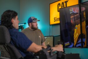 an instructor shows a student how to use a heavy equipment simulator