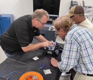 an instructor shows two students how to work on a fiber optic cable