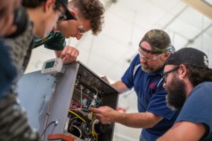 a man points to a machine wiring schematic as students look on