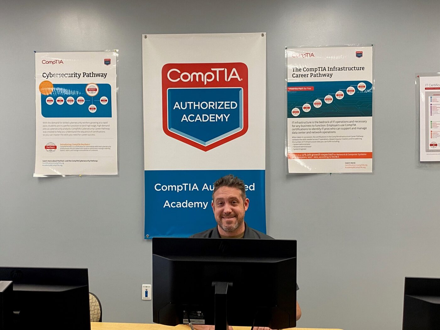 Aaron Winfree sitting behind computer with CompTIA posters in background