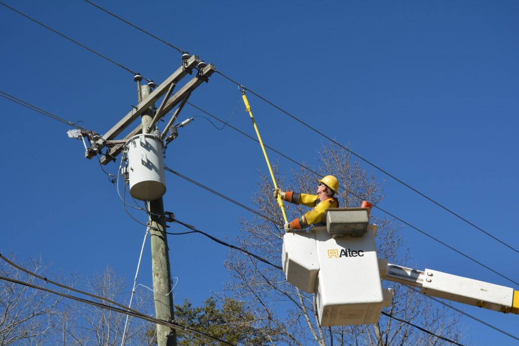 Power line worker in a bucket truck using an insulated pole to work on overhead electrical lines.