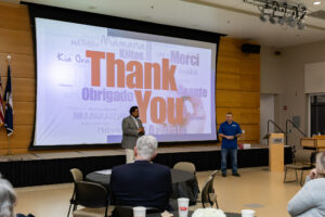 Two speakers stand at the front of a Laurel Ridge Community College event as a large presentation slide behind them displays the words “Thank You” in multiple languages.