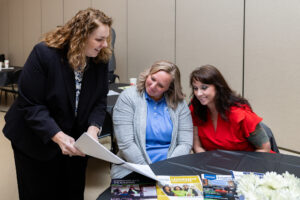 A woman points to a booklet and smiles while talking with two other women