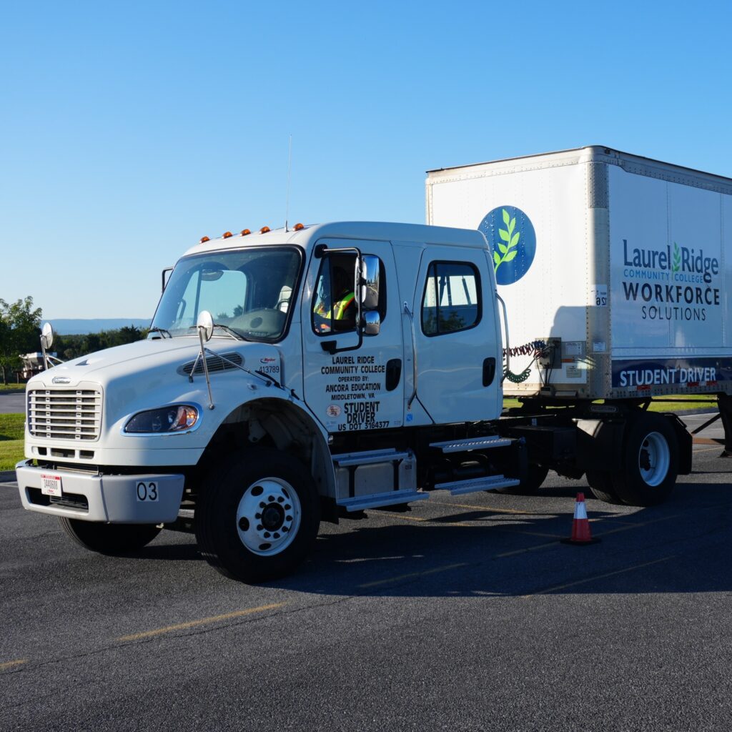A tractor trailer drives slowly in a parking lot, with wording on the trailer that says Laurel Ridge Workforce Solutions