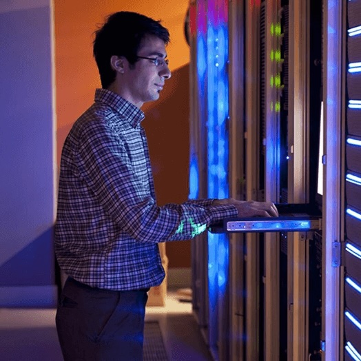 a man types on a computer inside of a computer server room