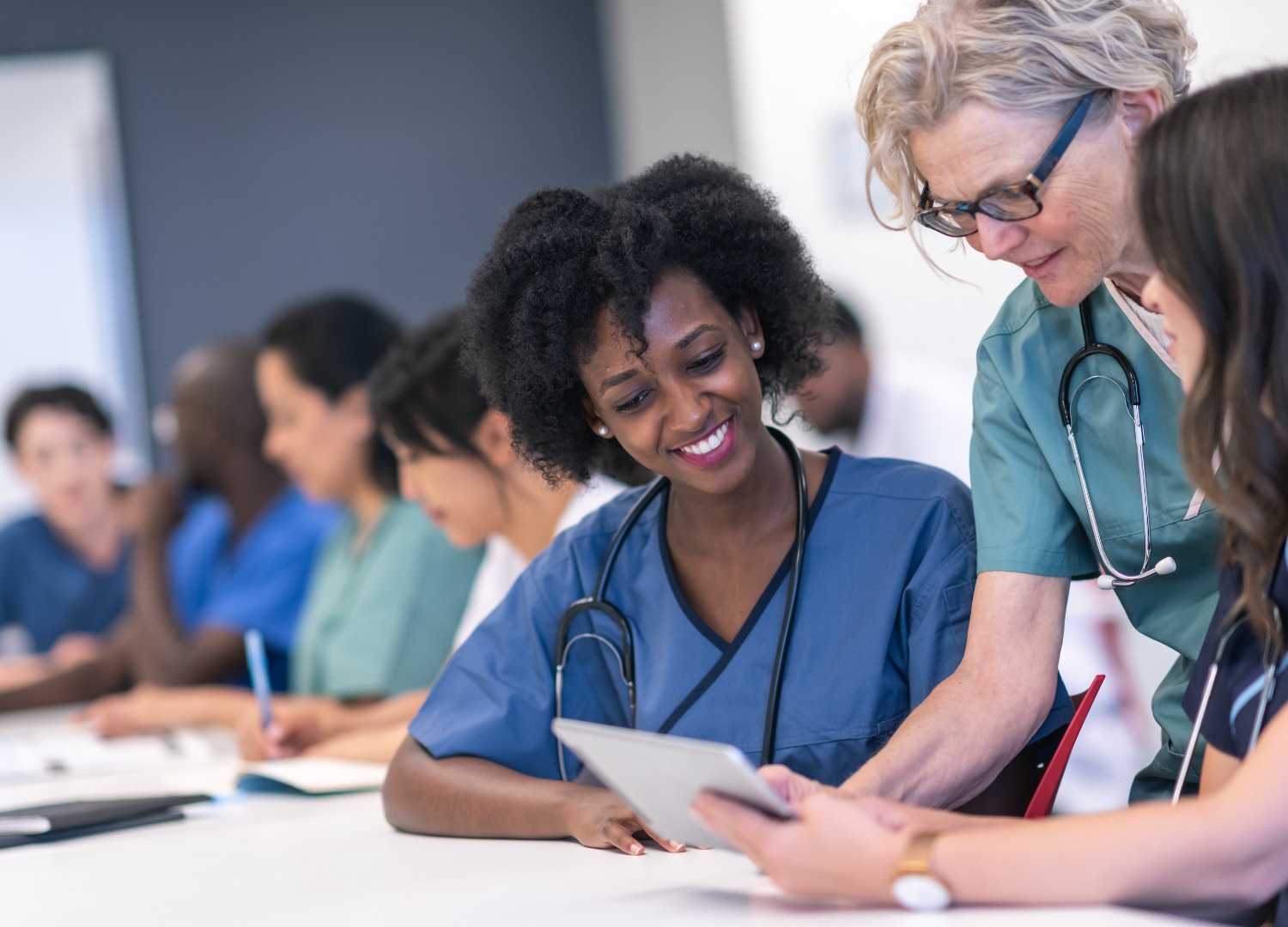 three women wearing medical scrubs look over documents while smiling